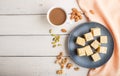 Traditional indian candy soan papdi in a blue ceramic plate with almond, pistache and a cup of coffee on a white wooden background Royalty Free Stock Photo