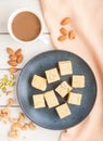 Traditional indian candy soan papdi in a blue ceramic plate with almond, pistache and a cup of coffee on a white wooden background Royalty Free Stock Photo