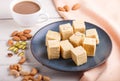 Traditional indian candy soan papdi in a blue ceramic plate with almond, pistache and a cup of coffee on a white wooden background Royalty Free Stock Photo