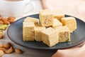 Traditional indian candy soan papdi in a blue ceramic plate with almond, pistache and a cup of coffee on a white wooden background Royalty Free Stock Photo