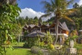 Traditional Indonesian style house next to a coconut palm tree in a tropical forest against a blue sky with clouds Royalty Free Stock Photo