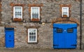 Traditional Irish stone hosue front with brick-framed windows and bright blue doors