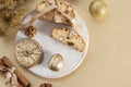 Traditional Italian biscotti cookies on a round white wooden board with walnuts and dried orange slices on a golden table near the