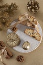 Traditional Italian biscotti cookies on a round white wooden board with walnuts and dried orange slices on a golden table near the