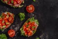 Traditional Italian Bruschetta with chopped tomatoes, mozzarella sauce, salad leaves and ham on a dark baton background. Royalty Free Stock Photo