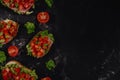 Traditional Italian Bruschetta with chopped tomatoes, mozzarella sauce, salad leaves and ham on a dark baton background. Royalty Free Stock Photo