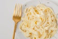 Traditional Italian pasta - Fetuccini Alfredo on a white table with golden appliances