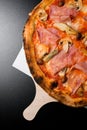 Traditional italian pizza with prosciutto, mushrooms and olives served on wooden board on black background. Royalty Free Stock Photo