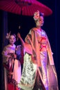 Actress in traditional kimono and fox mark gradually goes and her assistant holds umbrella above