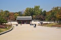 Traditional Korean Palace during Autumn, the light brown sand meets mountain and trees. Couple walking to enter the building.