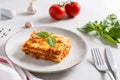 Traditional lasagna made with minced beef bolognese sauce and bechamel sauce topped with basil leaves on light background. Recipe