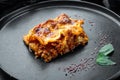 Traditional lasagna made with minced beef bolognese sauce topped with basil leafs, on plate, on black stone background Royalty Free Stock Photo