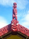Traditional Maori carved marae on house roof in red color under blue sky.