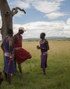 Traditional Masai men, talking in green field, one leaning against tree