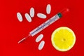 Traditional medical thermometer for measuring body temperature on a red background with pills and lemon. Royalty Free Stock Photo