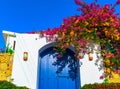 Traditional Mediterranean house with a stone fence and a large blue door decorated with flowering plants. Front bottom view