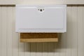 Traditional metal paper towel dispenser in a public bathroom, brown recycled paper towels, tan beadboard wall.