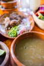 Traditional Mexican lamb broth and chopped meat in clay bowl and plates