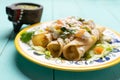 Mexican potato and cheese fried tacos also called flautas with green sauce on turquoise background