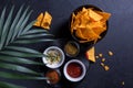 Traditional mexican snack nachos in a black plate with different sauces and spicy spices on a palm branch background. Black Royalty Free Stock Photo