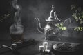 Traditional Moroccan teapot, with a steaming cup of tea, sugar and mint, in a smoky black atmosphere. Moroccan tea concept