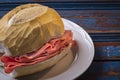 Traditional mortadella sandwich on a white plate and wooden table