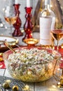 Traditional New Year salad Olivier in bowl on wooden table served with plates, glasses, bottle of wine, candles, garland, festive