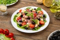 Traditional Nicoise salad in a white plate on an old rural table with sauce and ingredients. Selected focus.