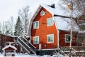 Traditional old big red wooden house in countryside. High long wooden porch leads to the second floor. Birch trees grow in the yar