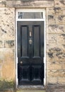 Traditional old black wooden door with brass letter box and knocker with a white frame surrounded by a stone wall Royalty Free Stock Photo