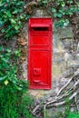 Traditional old English red postbox mounted in stone wall surrounded by ivy. Royalty Free Stock Photo