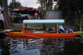 Traditional orange trajinera in Xochimilco lake with trees as background