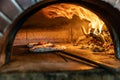 Traditional oven for baking pizza with burning wood and shovel. The cook rotates the pizza in the oven to ensure even baking Royalty Free Stock Photo