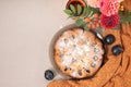 Traditional plum pie with sugar icing, orange knitted cloth, autumn flowers bouquet, plums on beige table background