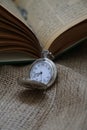 ancient pocket watch in front of an old book on a piece of cloth