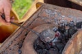 Traditional production of blacksmith`s work liquid silver metal melts in a leather black spoon on burning coals