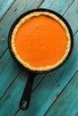 Traditional pumpkin pie minimalist style. Homemade bright colored tart in cast iron pan on blue background copyspace