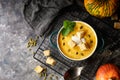 Traditional pumpkin soup puree with crackers, cream and seeds in a bowl, on a dark background