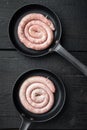 Traditional raw spiral pork sausages in cast iron frying pan  on black wooden table background  top view flat lay Royalty Free Stock Photo