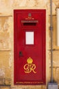 Traditional red vintage British postbox on a limestone building wall in Birgu, Malta