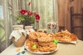 Table in rustic house, on which there are plates with buns, pies and pretzels, samovar, clay jugs with milk, and vase with bouquet Royalty Free Stock Photo