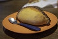 Traditional savory pastry of Cochabamba called saltena on an orange plate with a spoon