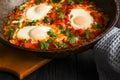 Traditional shakshuka with eggs, tomato, and parsley in a iron pan on a dark background.