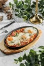 Traditional shakshuka with eggs, tomato, and parsley in a iron pan on light marble background. Healthy sea food, hard light,