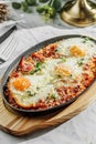 Traditional shakshuka with eggs, tomato, and parsley in a iron pan on light marble background. Healthy sea food, hard light,