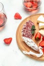 Traditional Spanish Fuet thin dried sausage with Camembert cheese, strawberries and glass rose wine on white background. vertical Royalty Free Stock Photo
