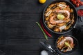 Traditional spanish seafood paella in pan and bowl with rice, peas, shrimps, mussels and squid on black wooden planks, top view Royalty Free Stock Photo