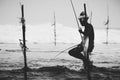 Traditional Stilt fishermen silhouette, fishing rod, and a bag for collecting fish, sitting on a stick cross above the seawater