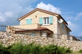 Traditional stone wall with wrought iron fence on top in front of modern Mediterranean villa with new facade and open blue wooden Royalty Free Stock Photo