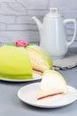 Traditional Swedish dessert Princess cake with green marzipan cover and pink rose decoration, sliced, on gray background, vertical